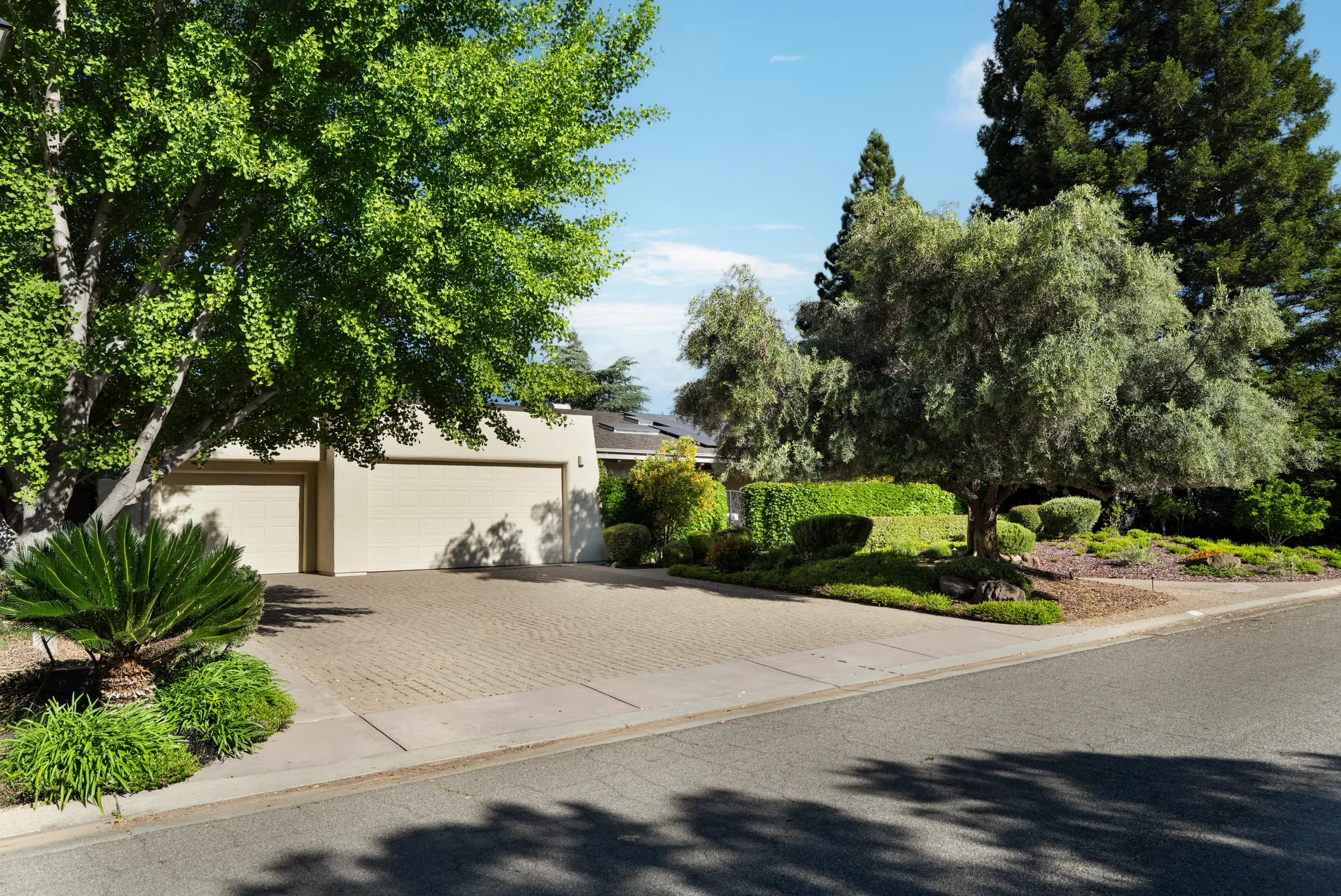 A single-story house behind clipped hedges, with an olive tree, a gravel court and a deep colonnade. Frame 3 of 25.