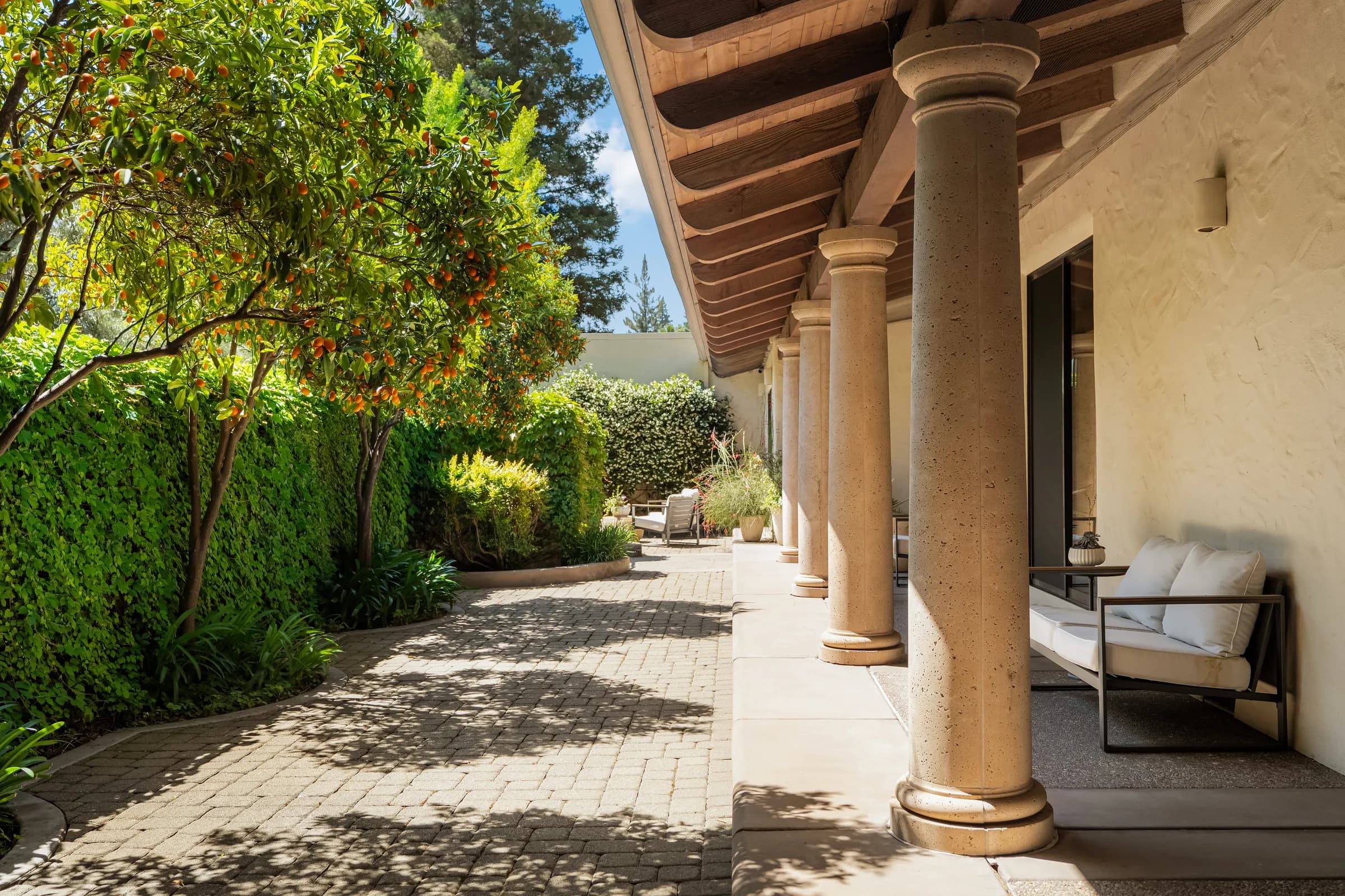 A deep colonnade running the length of the elevation, its columns throwing bars of shade onto the gravel.