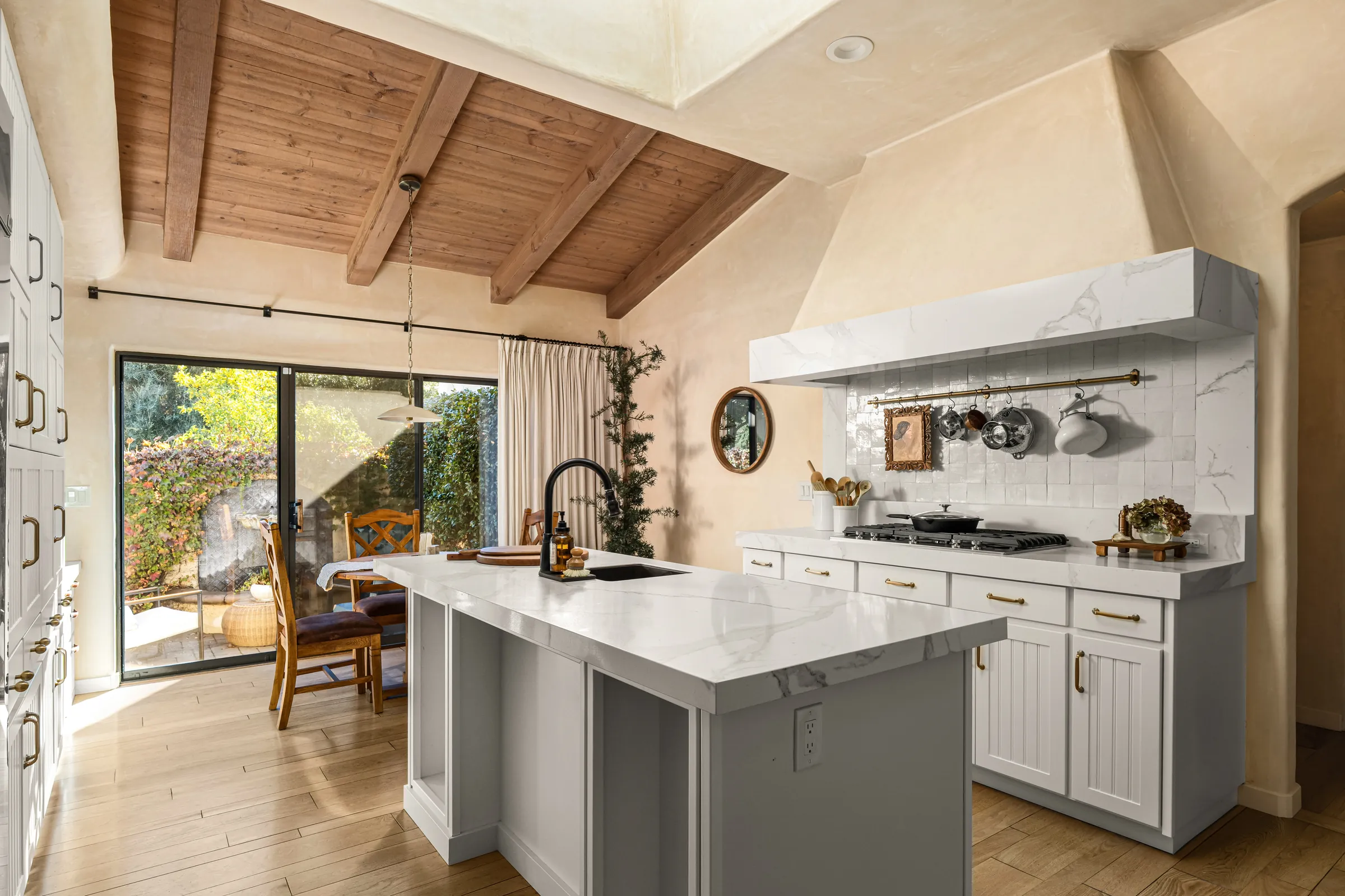 A kitchen under an open beamed ceiling, the island lit from a run of glass on the garden side.