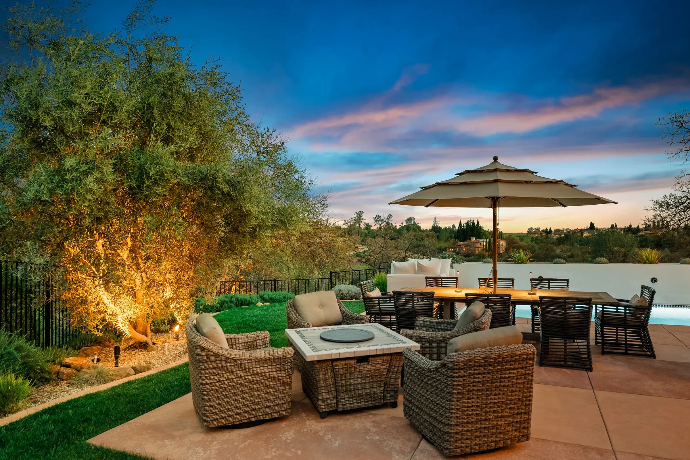 A terrace at dusk, umbrellas up and a fire table lit, the sky still holding color.