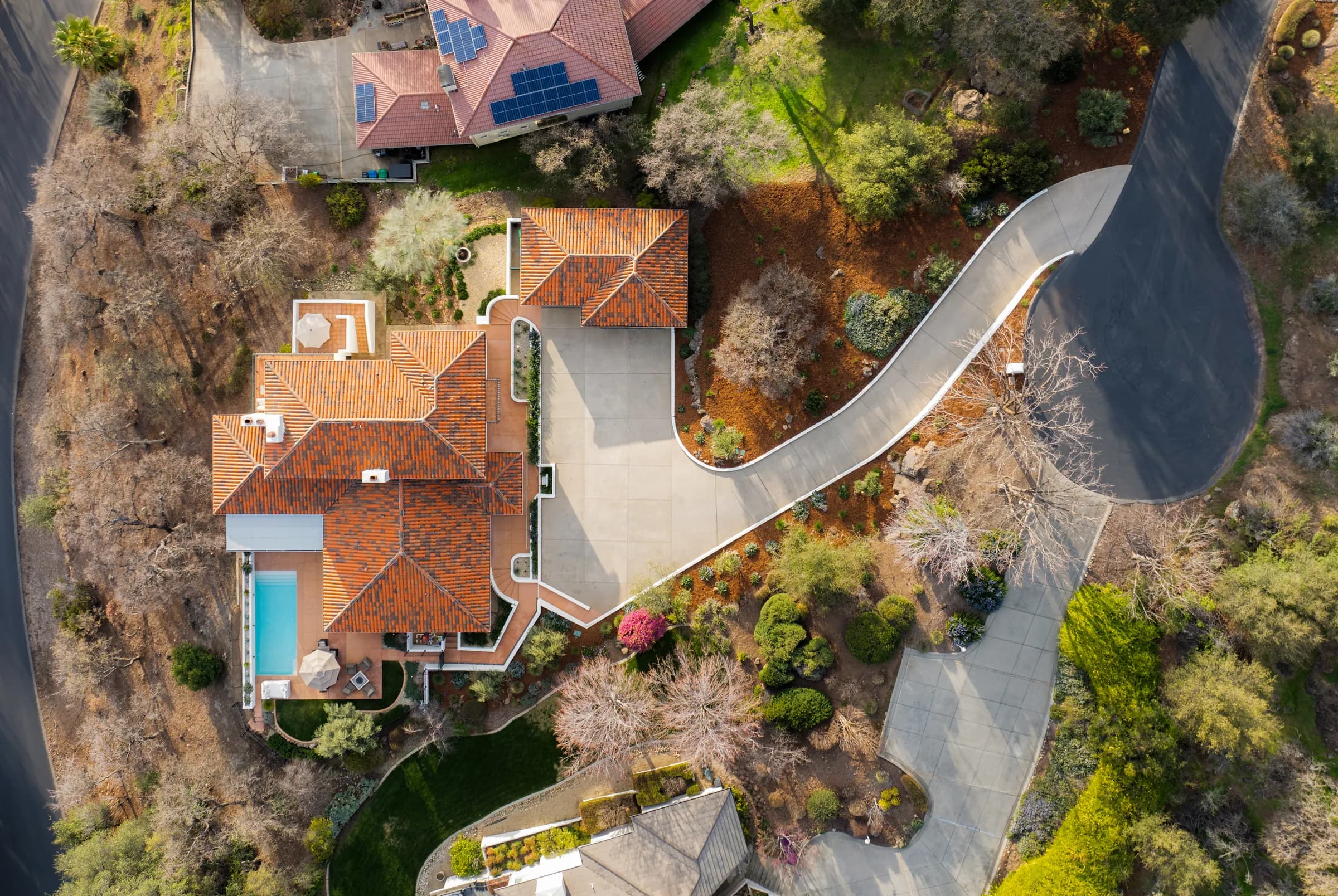 A tile-roofed estate from the air, its drive curving down through blossom and mature planting to a pool terrace.