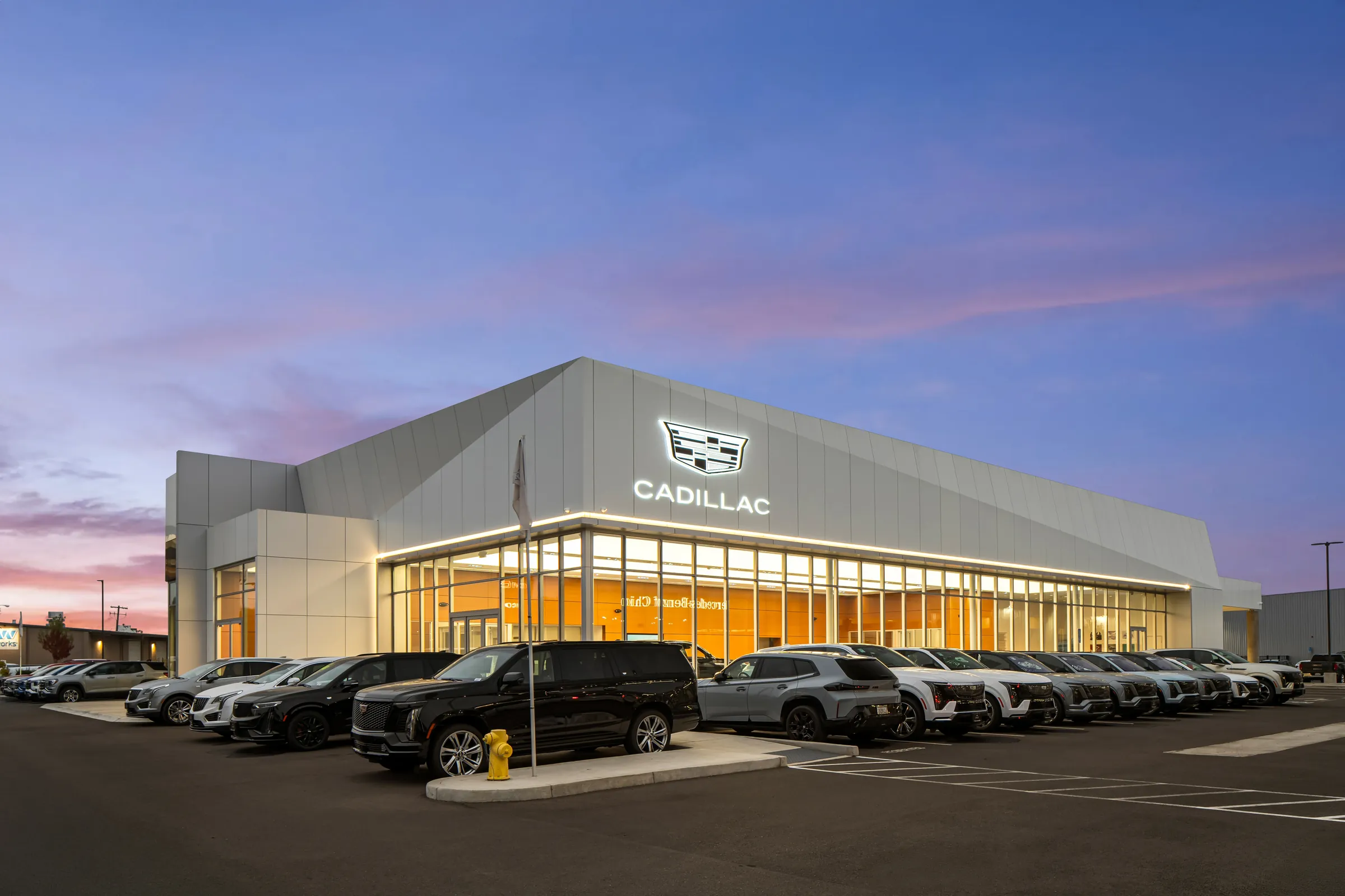 Automotive dealership exteriors at dusk and the showroom interiors behind them. Frame 3 of 6.